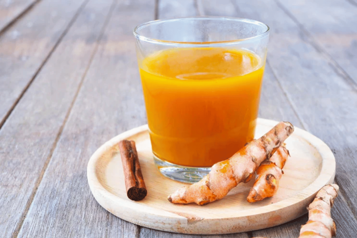 Turmeric latte in a glass with turmeric roots and a cinnamon stick on a wooden platter